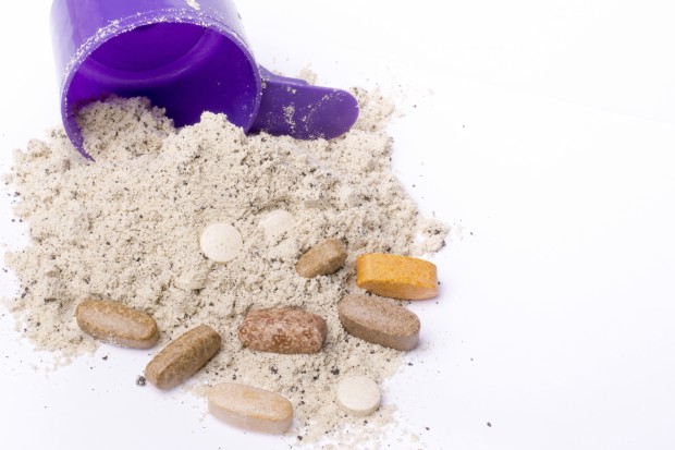 Whey protein powder in scoop with vitamins and violet plastic shaker
